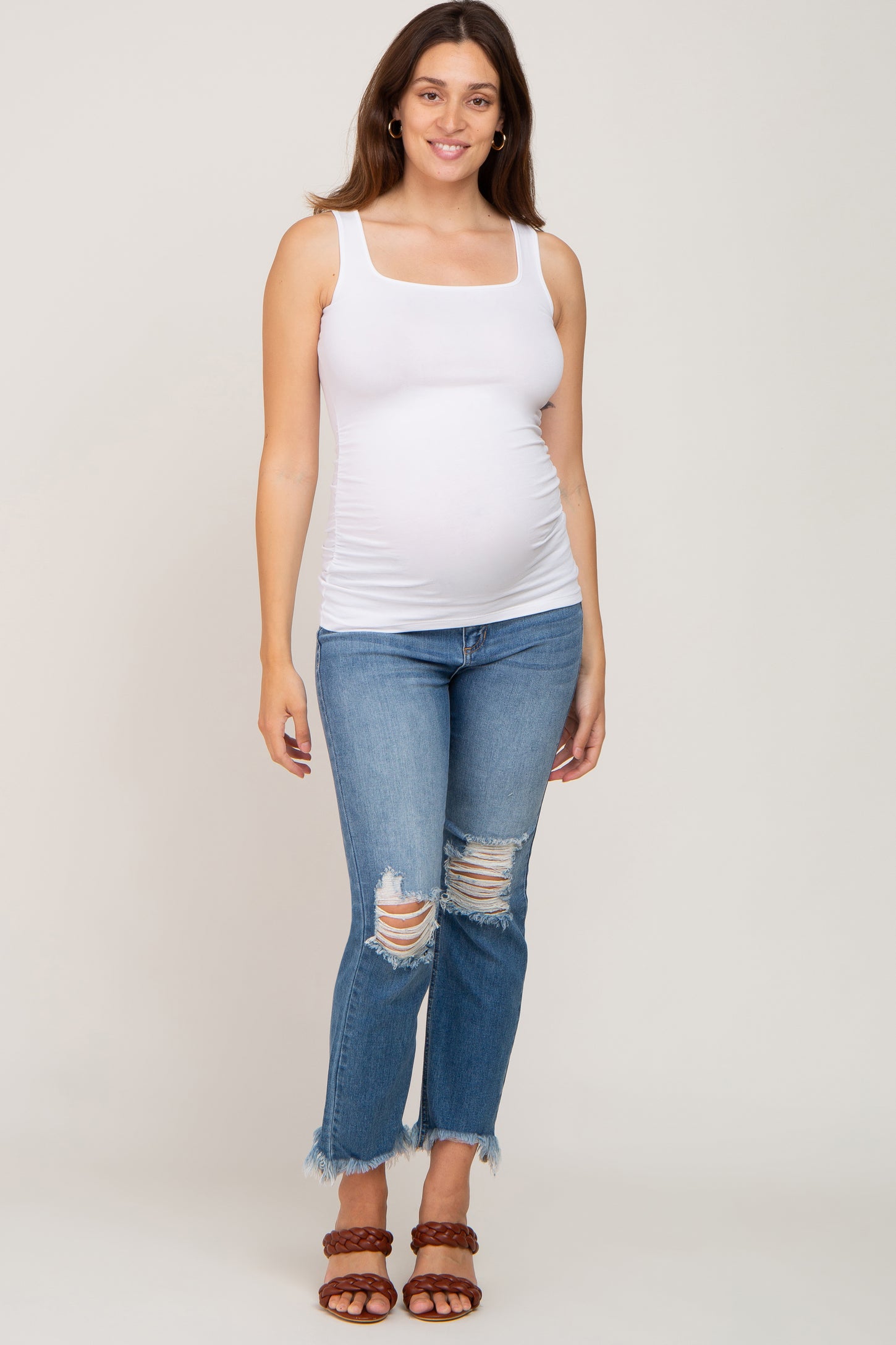 woman wearing a white maternity tank top and distressed blue jeans, showing her baby bump