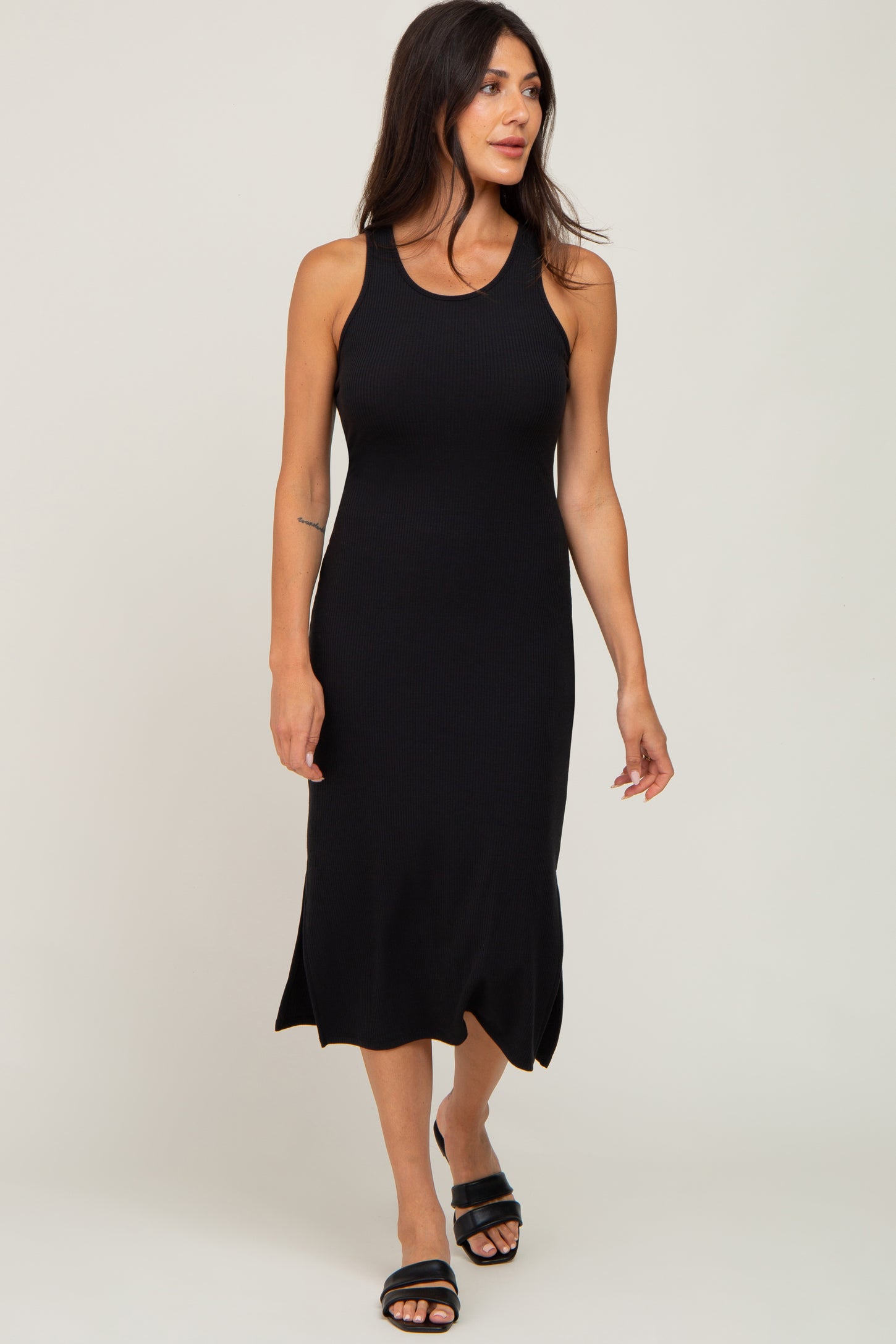 woman wearing a black ribbed sleeveless midi dress and black slide sandals against a white background