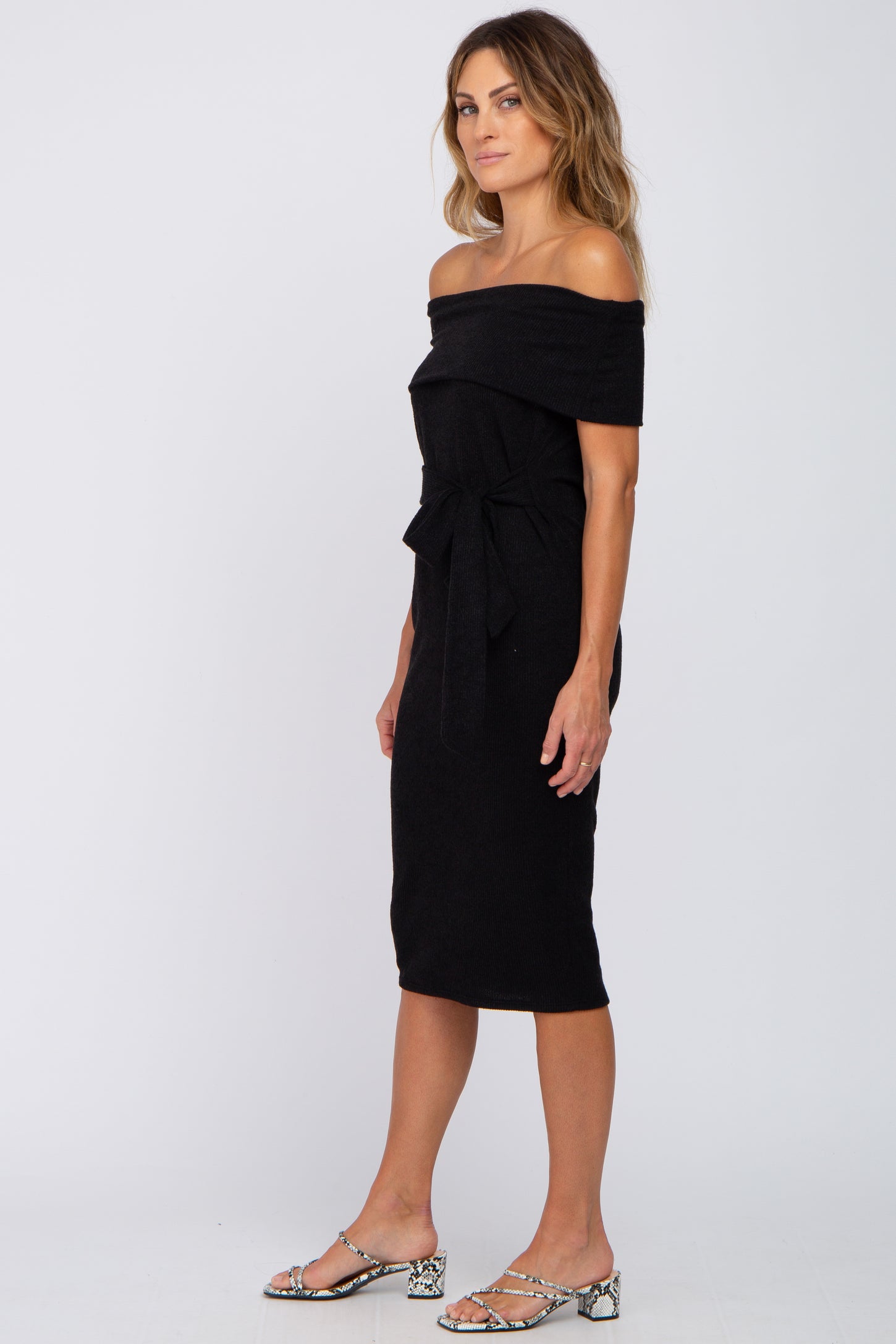 woman wearing a black off-the-shoulder midi dress with a waist tie and snakeskin print sandals