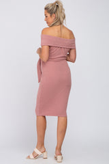 Woman wearing a mauve off-the-shoulder ribbed maternity midi dress with a waist tie and block heel sandals