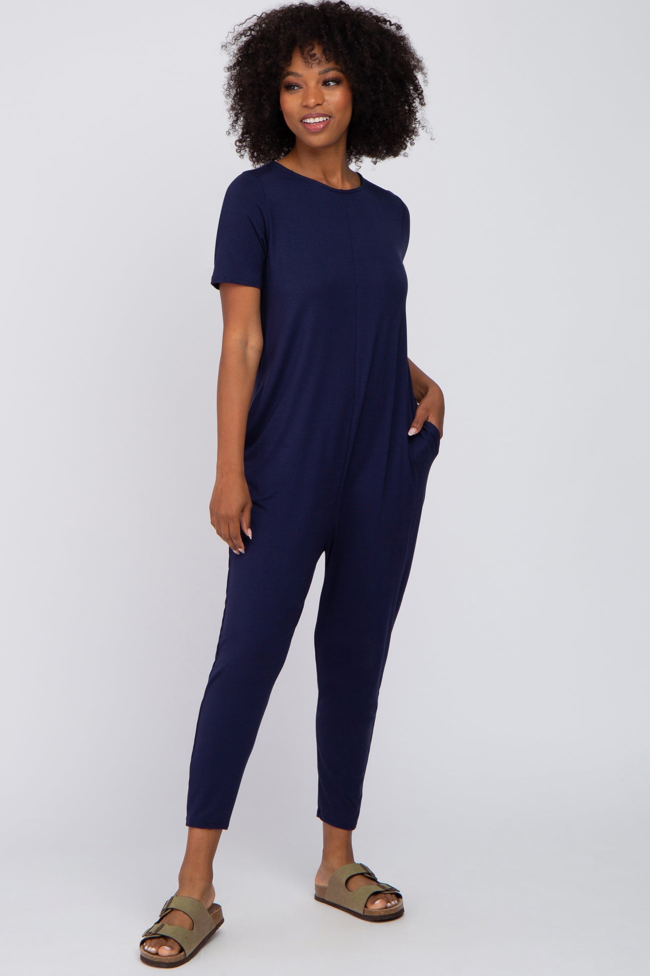 woman wearing a dark navy short sleeve jumpsuit with side pockets and styled with green sandals