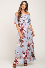 woman wearing a light blue off-the-shoulder floral maternity maxi dress with a flowing skirt and standing comfortably
