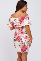 Woman wearing a white off-the-shoulder maternity dress with a pink floral print and ruffle neckline