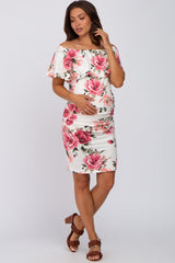 woman wearing a white off-shoulder maternity dress with pink floral print, holding her baby bump