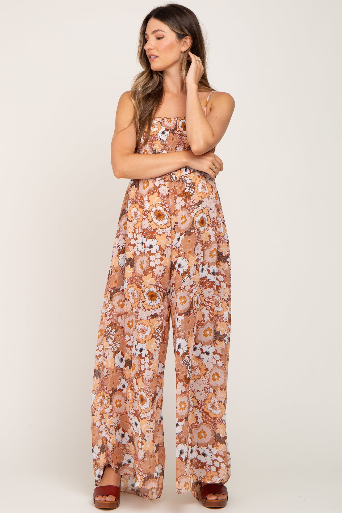 woman wearing a brown floral print wide leg jumpsuit with smocked bodice and platform sandals