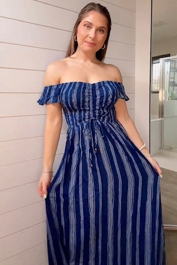 woman wearing a navy blue off-the-shoulder maxi dress with striped pattern and adjustable tie detail
