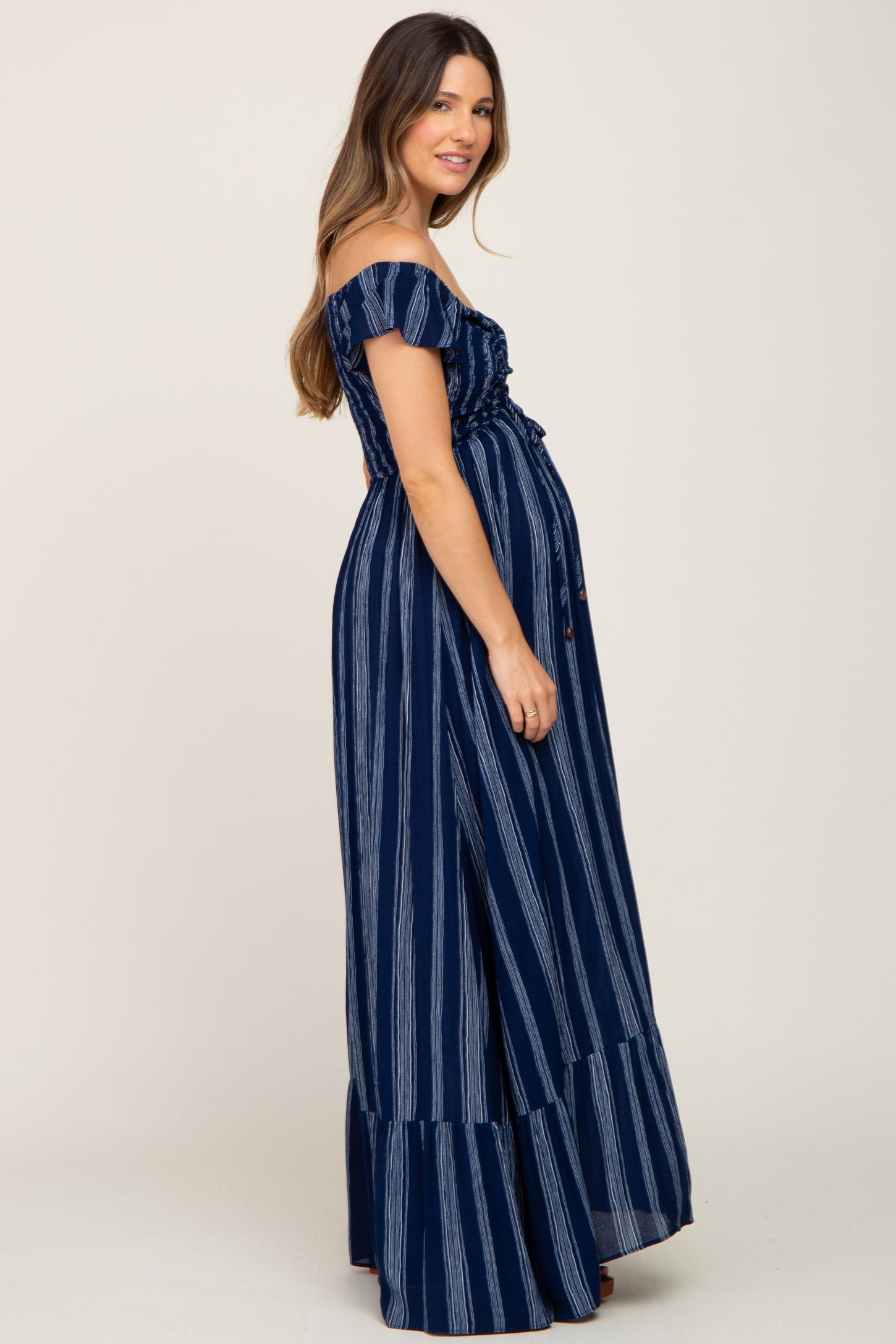 woman wearing a navy blue striped off-the-shoulder maternity maxi dress with a fitted bodice and flowing skirt, showing baby bump