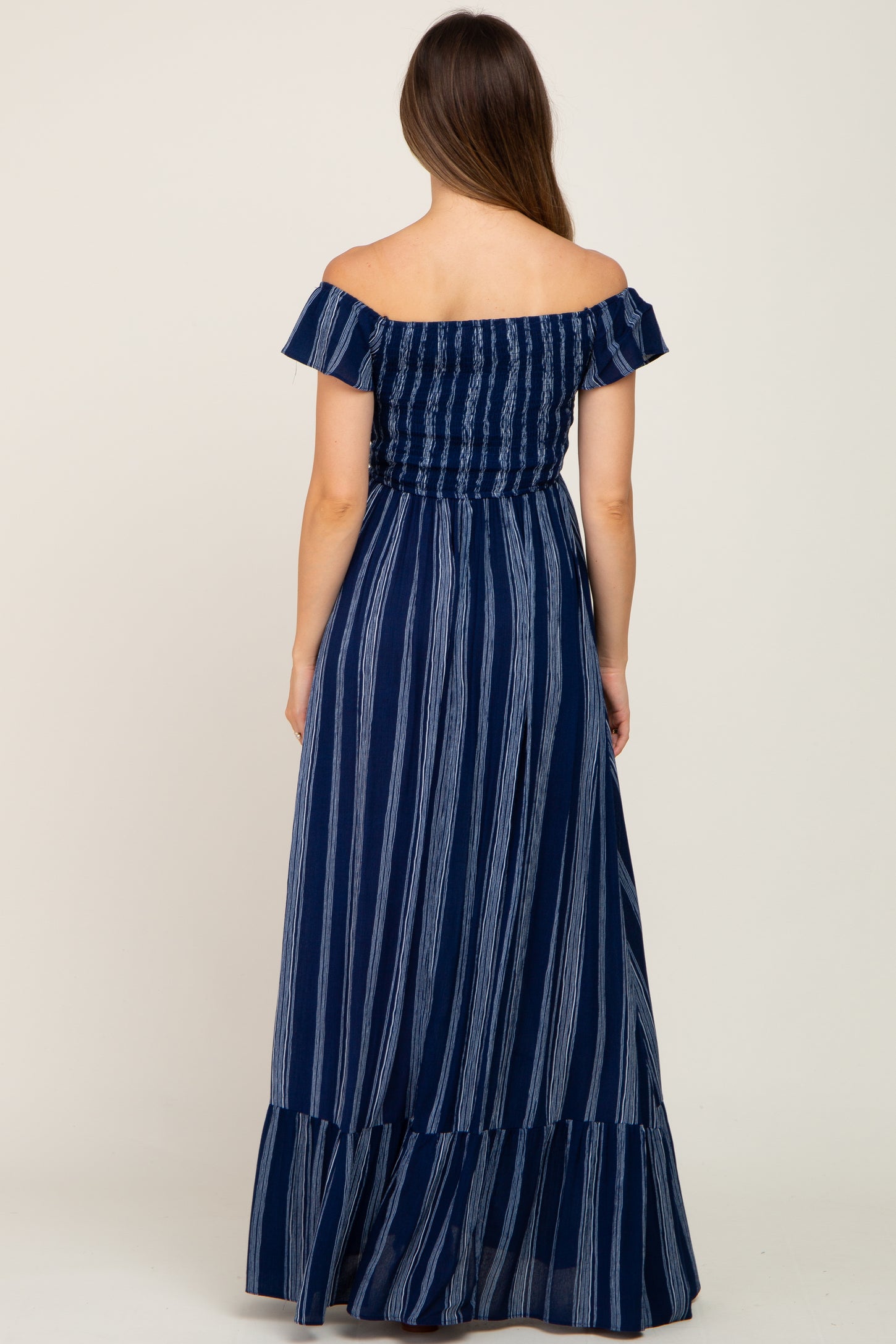 woman wearing a navy blue striped off-the-shoulder maternity maxi dress, showing the back view and a flowing skirt