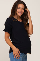 smiling pregnant woman wearing a black short puff sleeve maternity top and blue jeans