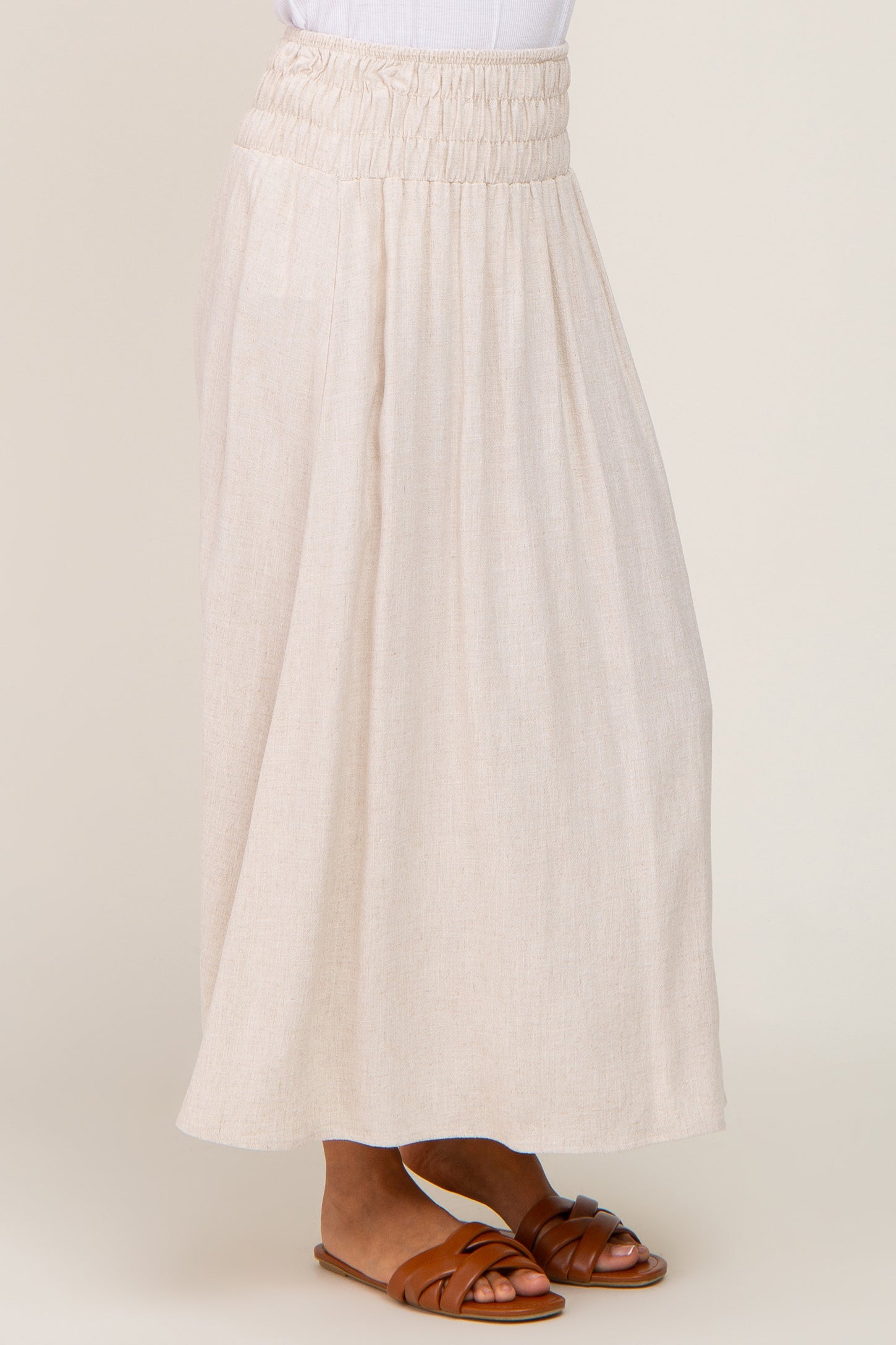 woman wearing a beige linen maxi skirt with a smocked waistband and brown leather sandals