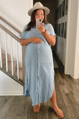 woman wearing a light blue button-up maternity maxi dress, holding her baby bump, with a hat and sandals