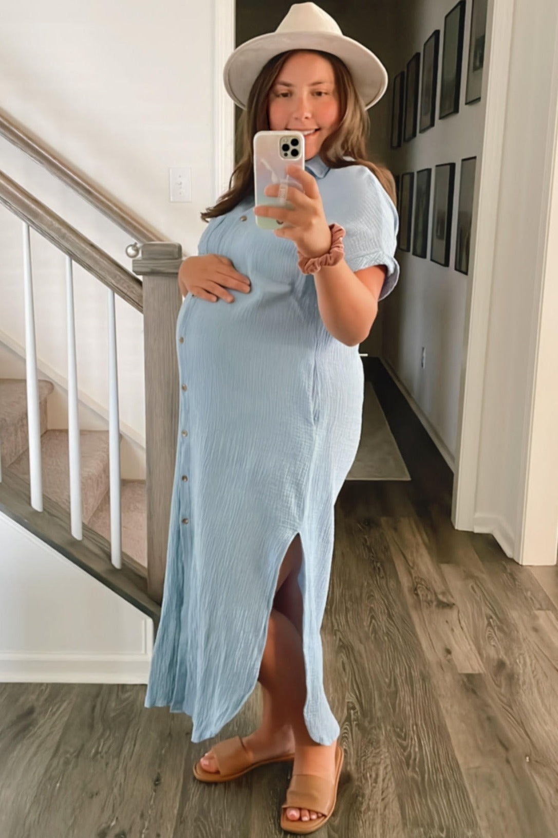 woman wearing a light blue maternity maxi dress with buttons and a side slit, holding her baby bump while standing indoors