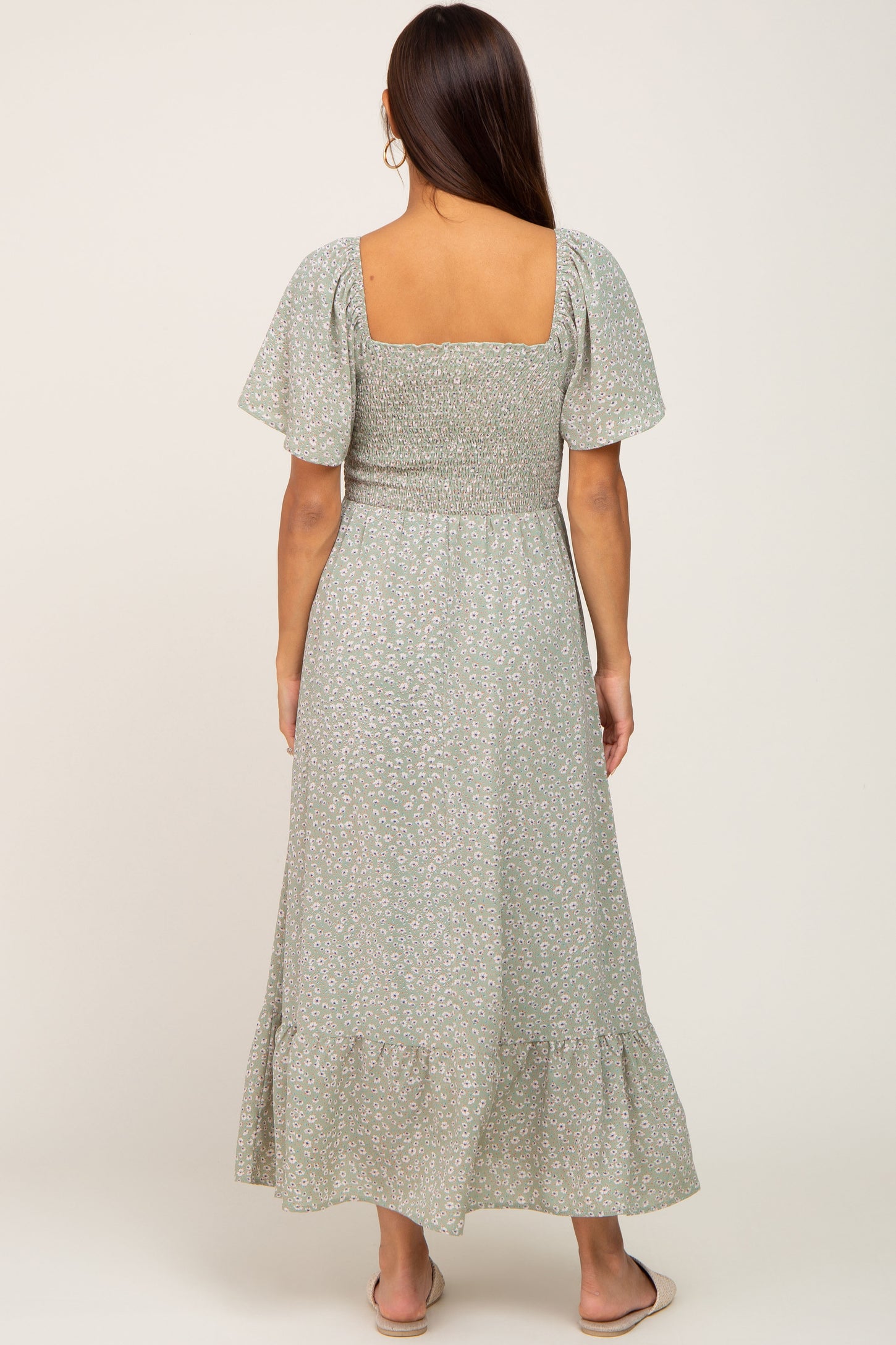 Back view of a woman wearing a sage green floral smocked maxi dress with flutter sleeves and a square neckline