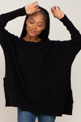 woman wearing a black oversized knit sweater with side pockets and a relaxed fit, smiling while raising her hands