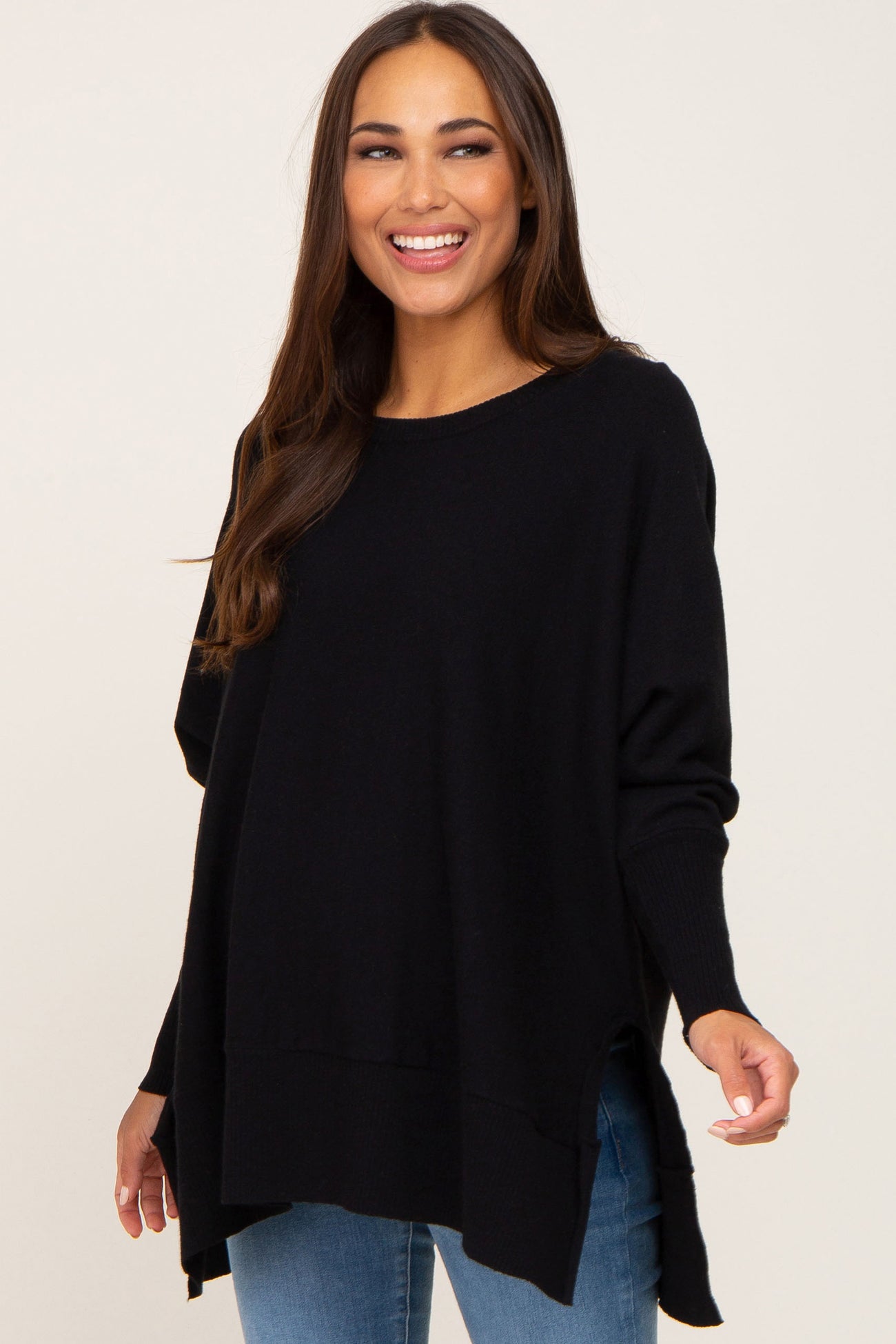 woman wearing a black long sleeve maternity sweater with a relaxed fit and side slits, smiling at the camera