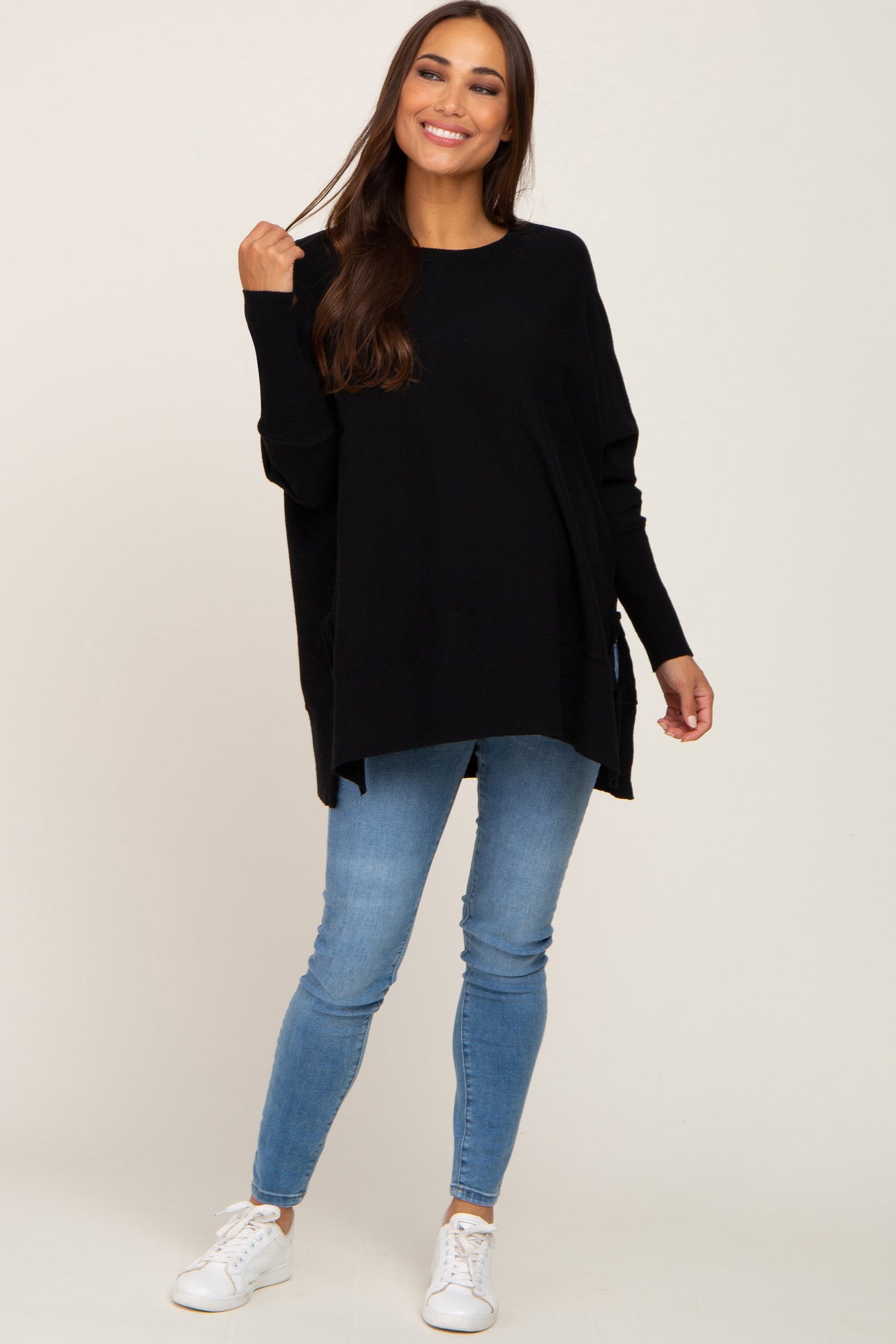 woman wearing oversized black knit sweater and blue skinny jeans with white sneakers
