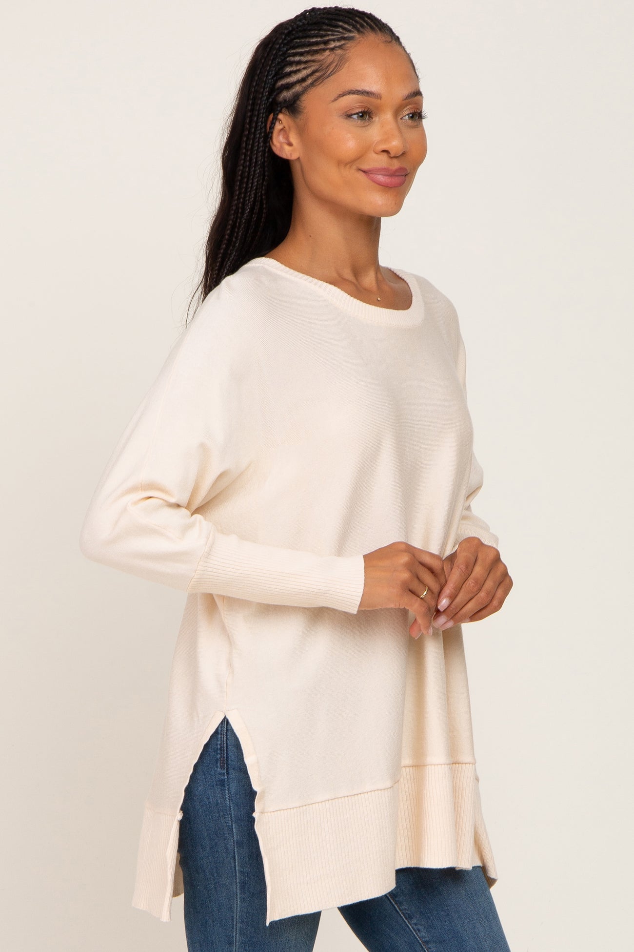 woman wearing a cream long sleeve oversized sweater with side slits and a relaxed fit, paired with blue jeans