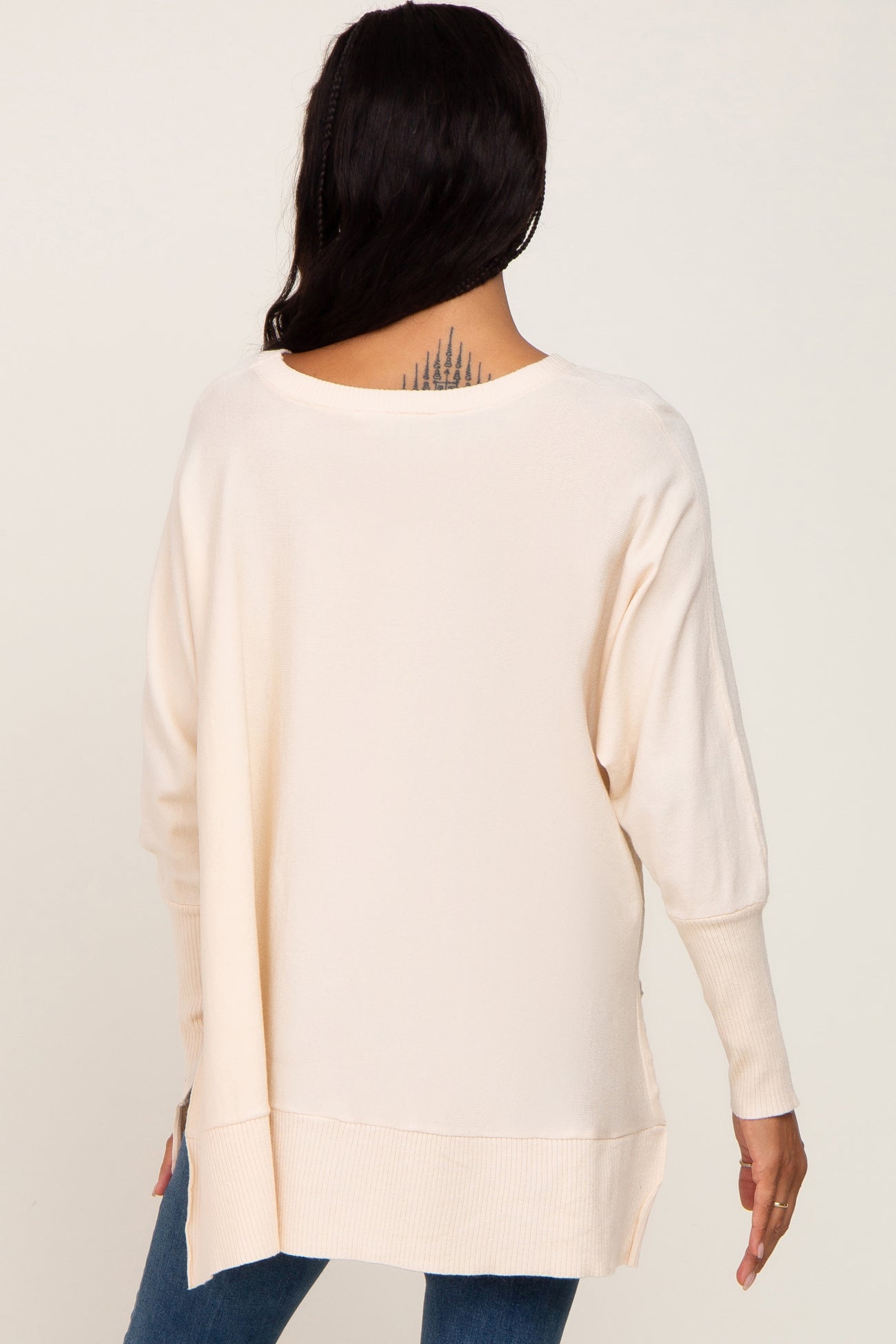 woman wearing a light beige oversized sweater with a scooped neckline and ribbed details