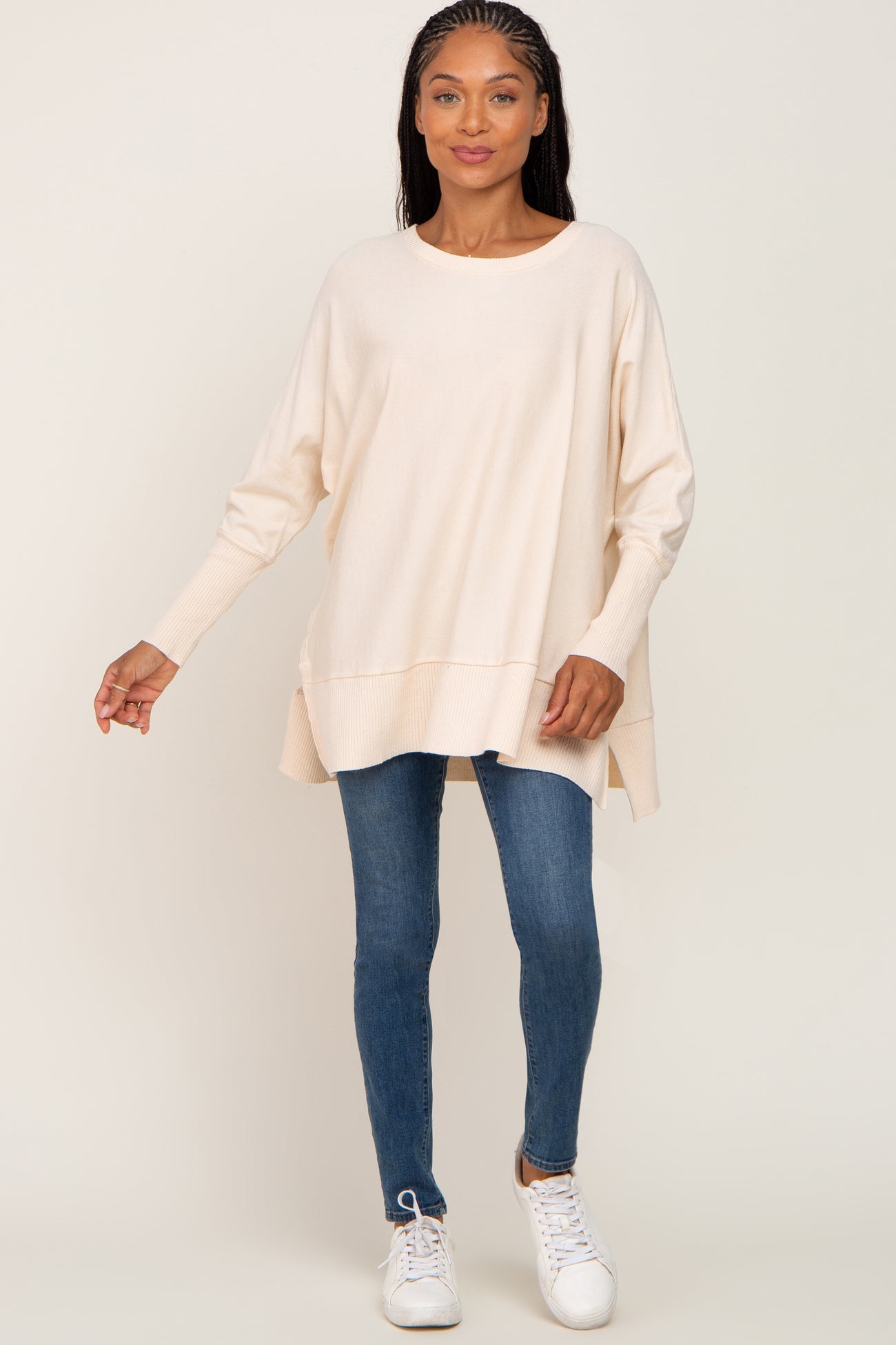 woman wearing a creamy beige oversized sweater with ribbed detailing and blue skinny jeans, paired with white sneakers
