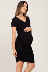 woman wearing a black short sleeve maternity dress with ruched side details and a visible baby bump