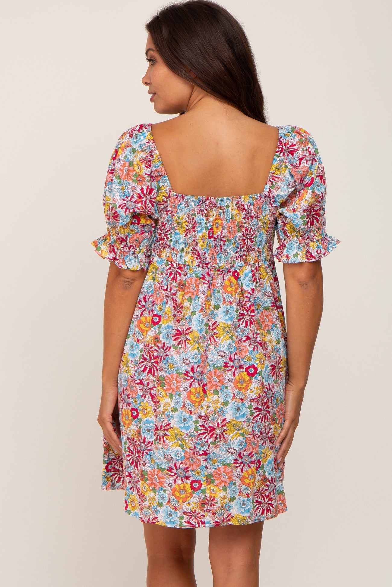 Back view of woman wearing a colorful floral print mini dress with smocked back and puff sleeves