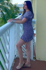 woman in purple floral mini dress standing on a balcony with palm trees in the background