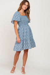 woman wearing a blue floral smocked maternity dress with flutter sleeves and white heels