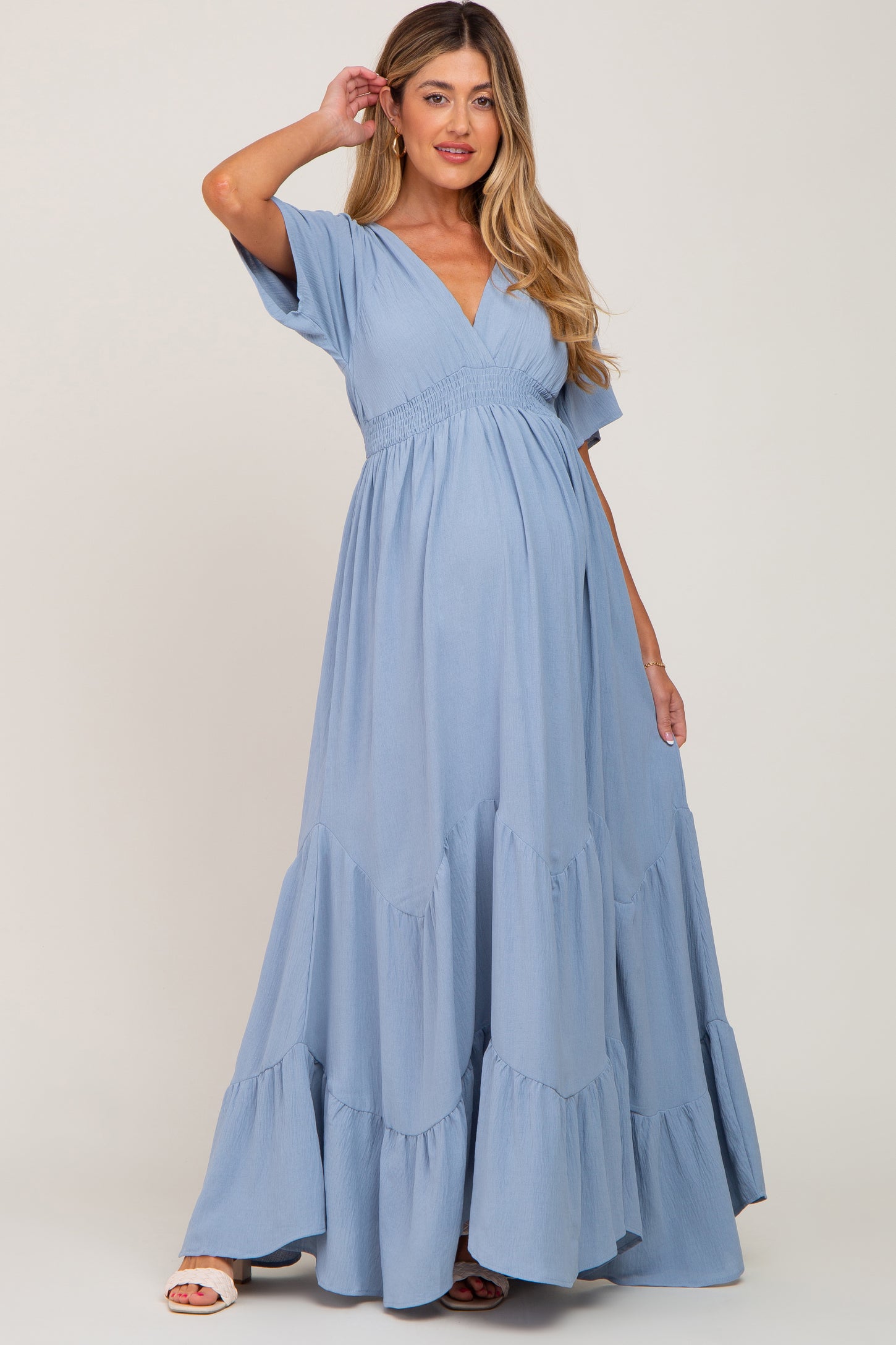 woman wearing a light blue tiered maternity dress with a v-neckline and short sleeves, showcasing her baby bump