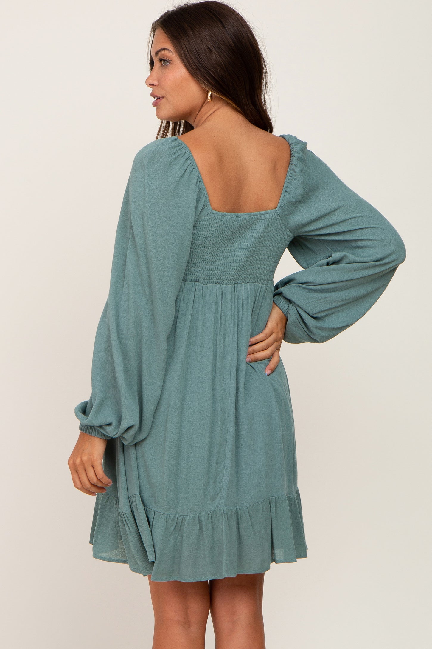 woman wearing a teal maternity dress with long sleeves and a smocked back, showcasing a flowing skirt and ruffled hem