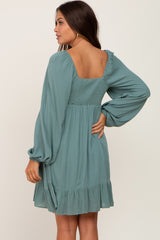 woman wearing a teal maternity dress with long sleeves and a smocked back, showcasing a flowing skirt and ruffled hem