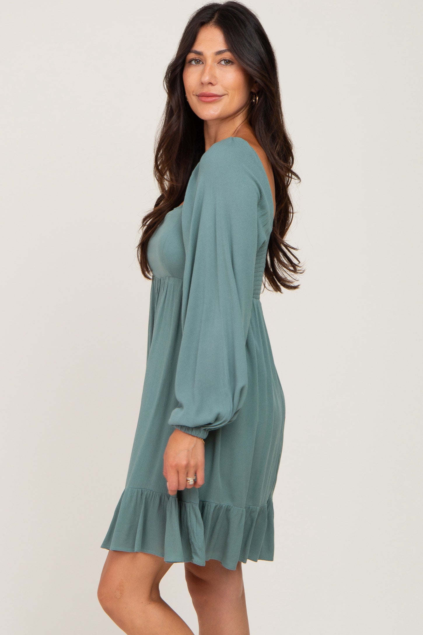 woman wearing a teal long sleeve dress with a ruffled hem and a fitted bodice