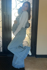 pregnant woman in light wash denim maternity overalls and white long sleeve shirt posing in front of a door