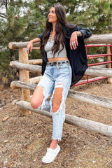 woman wearing a gray cropped tank top, distressed light wash jeans, and a black oversized shirt, sitting on a fence