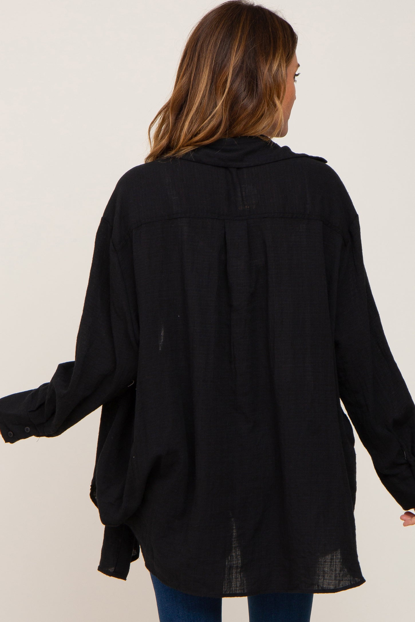 woman wearing a loose black button-up shirt, seen from the back, with long sleeves and a relaxed fit