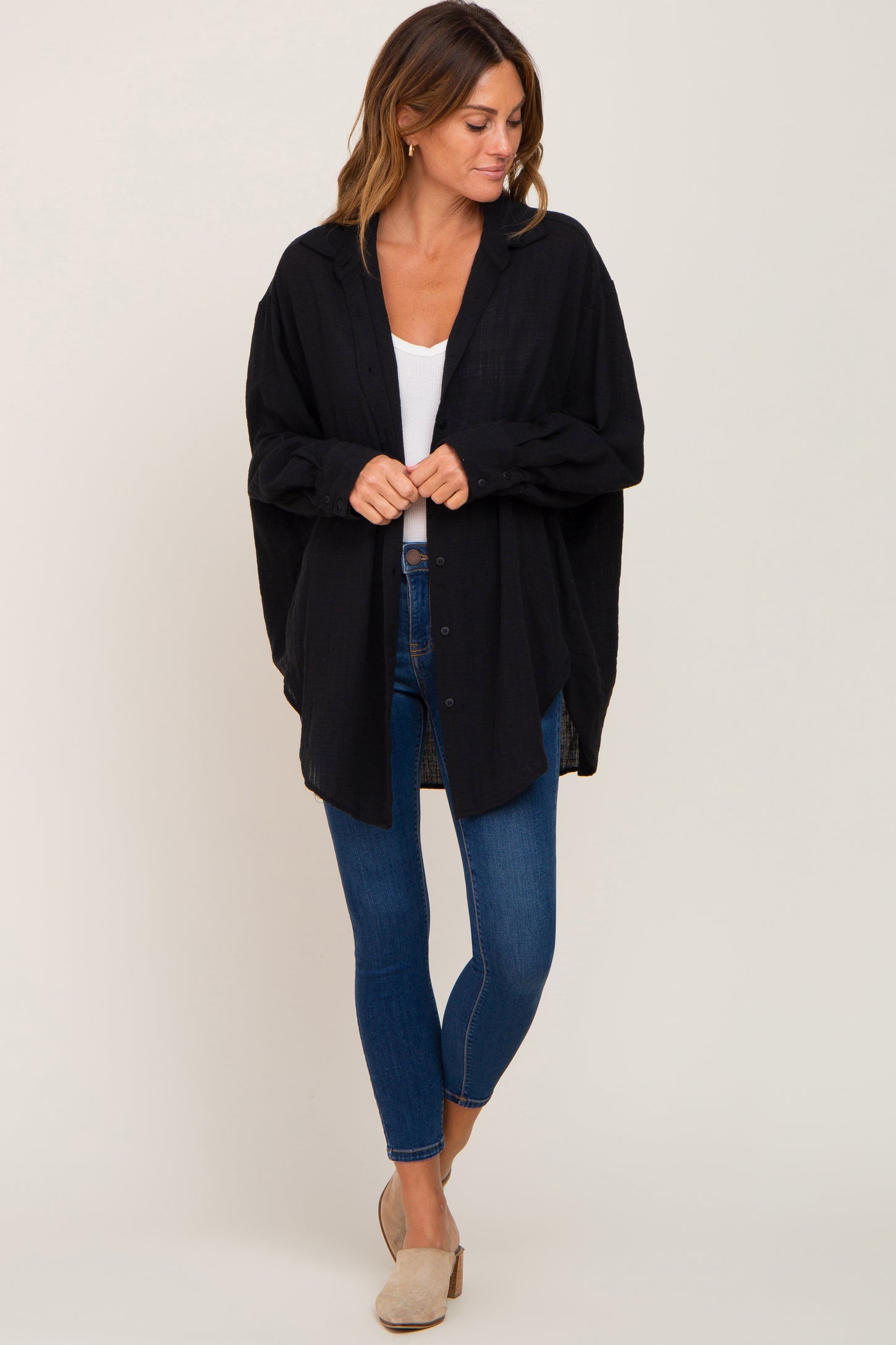 woman wearing a black oversized button-up shirt, white tank top, and blue jeans, standing with hands clasped in front