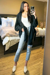 woman wearing a black oversized jacket, white tank top, and light blue ripped jeans, posing in front of a mirror