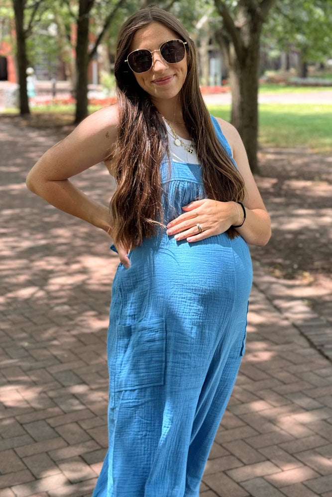 pregnant woman in blue maternity jumpsuit and sunglasses posing outdoors on a brick path