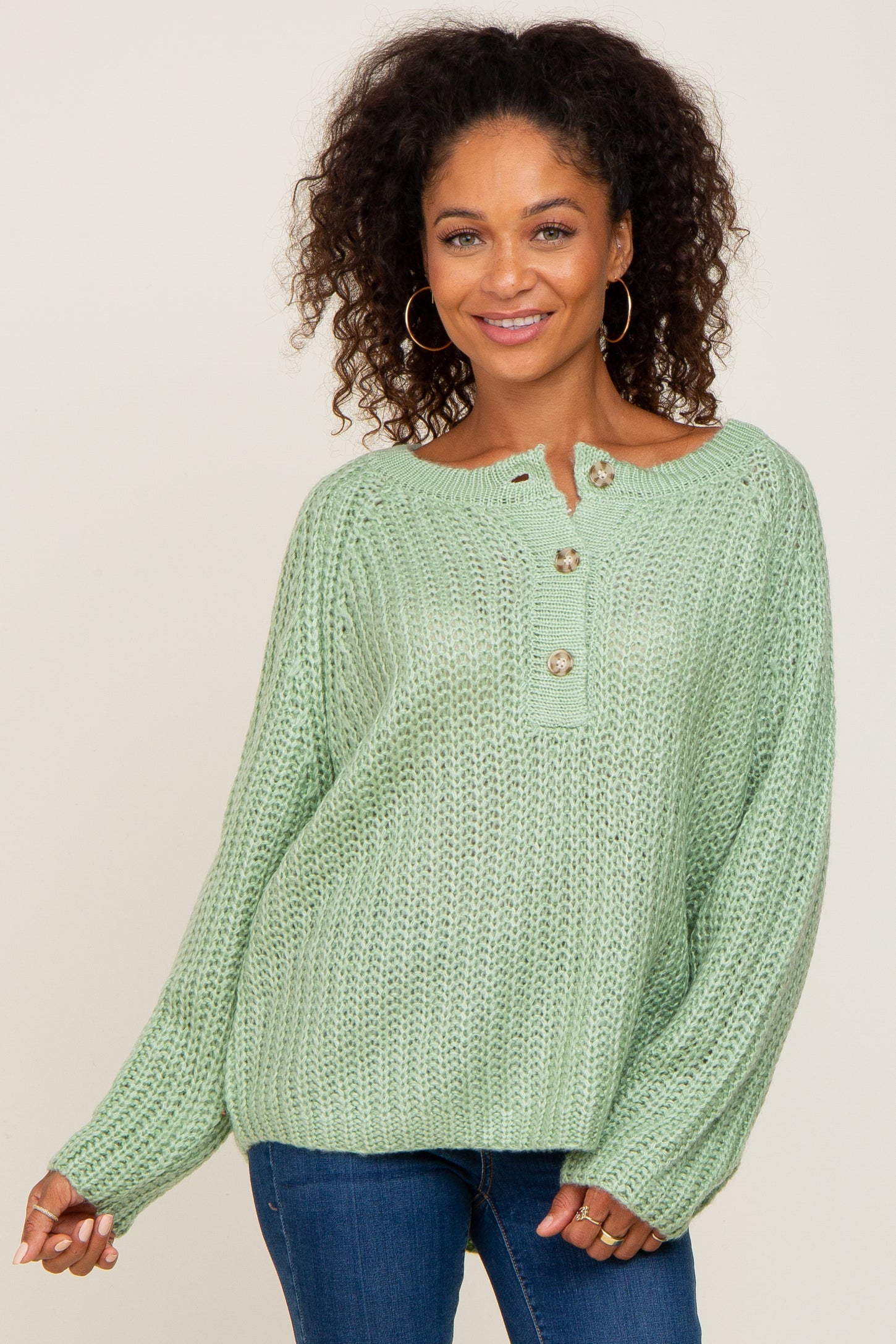 woman with curly hair wearing a light green knit henley sweater and blue jeans