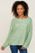 woman with curly hair wearing a light green knit henley sweater and blue jeans