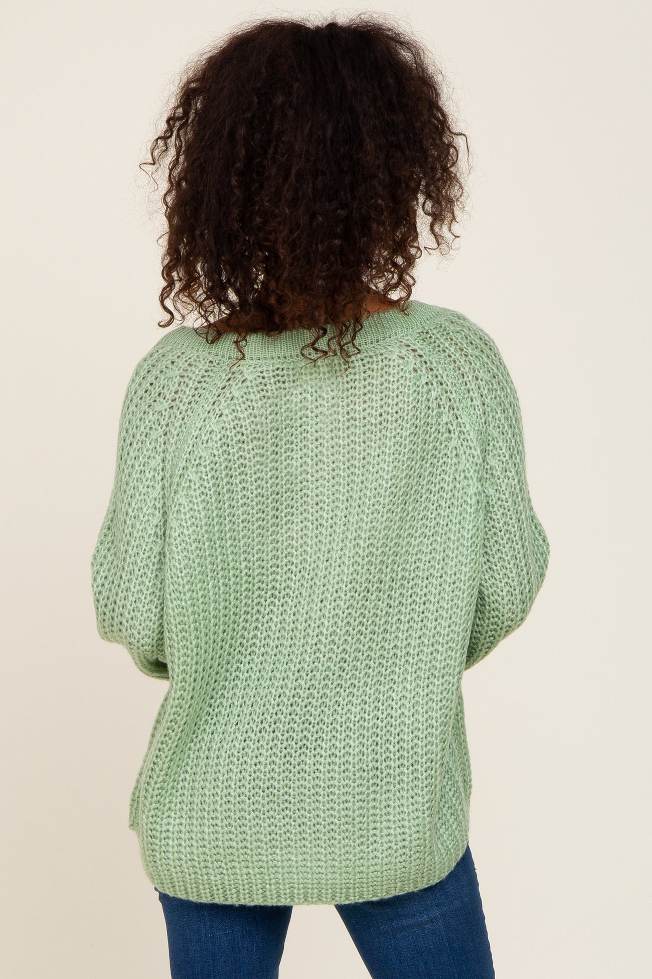 Back view of a person with curly hair wearing a light green chunky knit sweater and blue jeans