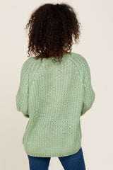 Back view of a person with curly hair wearing a light green chunky knit sweater and blue jeans