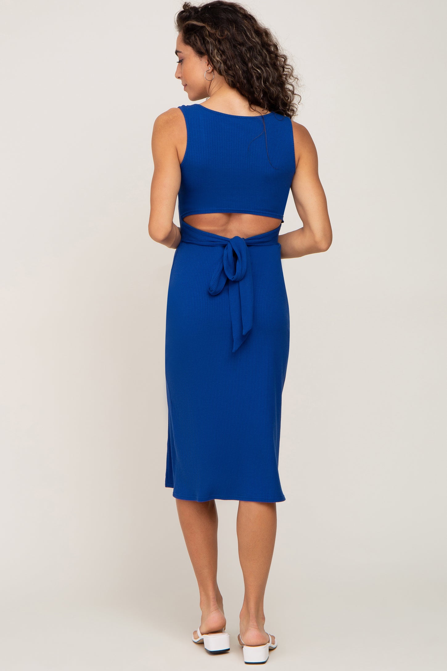 woman wearing a blue ribbed dress with a back cutout and tie detail, viewed from the back