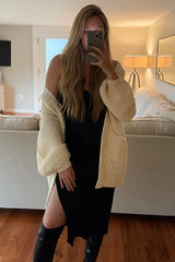 woman in black slit dress and cream chunky knit cardigan taking mirror selfie in living room