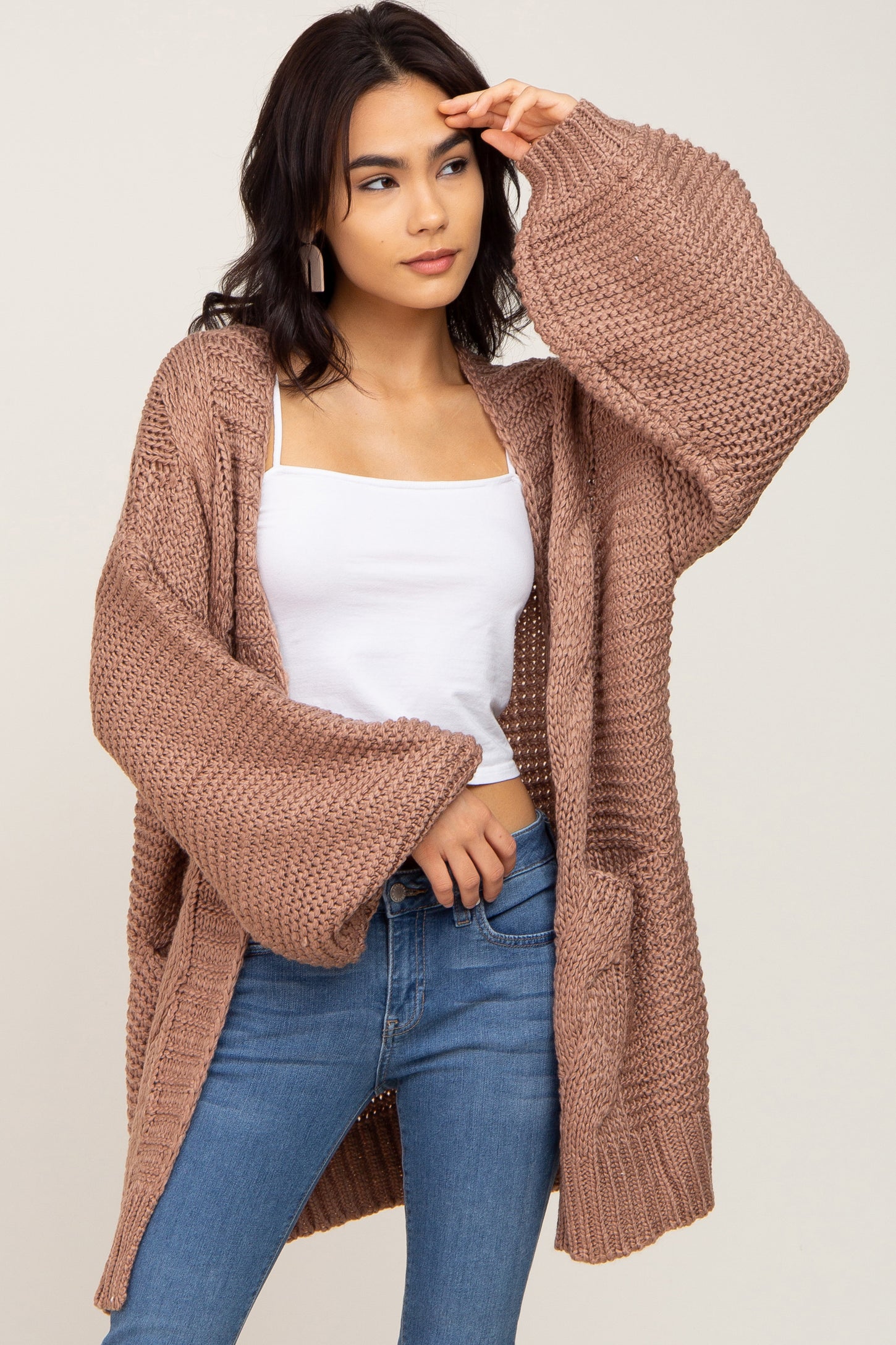 Woman wearing a mauve oversized chunky knit cardigan with bell sleeves, white tank top, and blue jeans