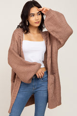 Woman wearing a mauve oversized chunky knit cardigan with bell sleeves, white tank top, and blue jeans