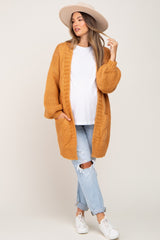 woman wearing a mustard yellow cable knit maternity cardigan with a white t-shirt and distressed jeans