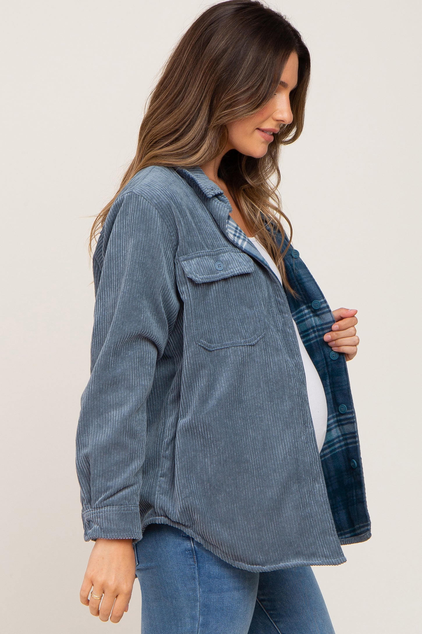 Pregnant woman wearing a blue corduroy maternity shacket with plaid lining and blue jeans