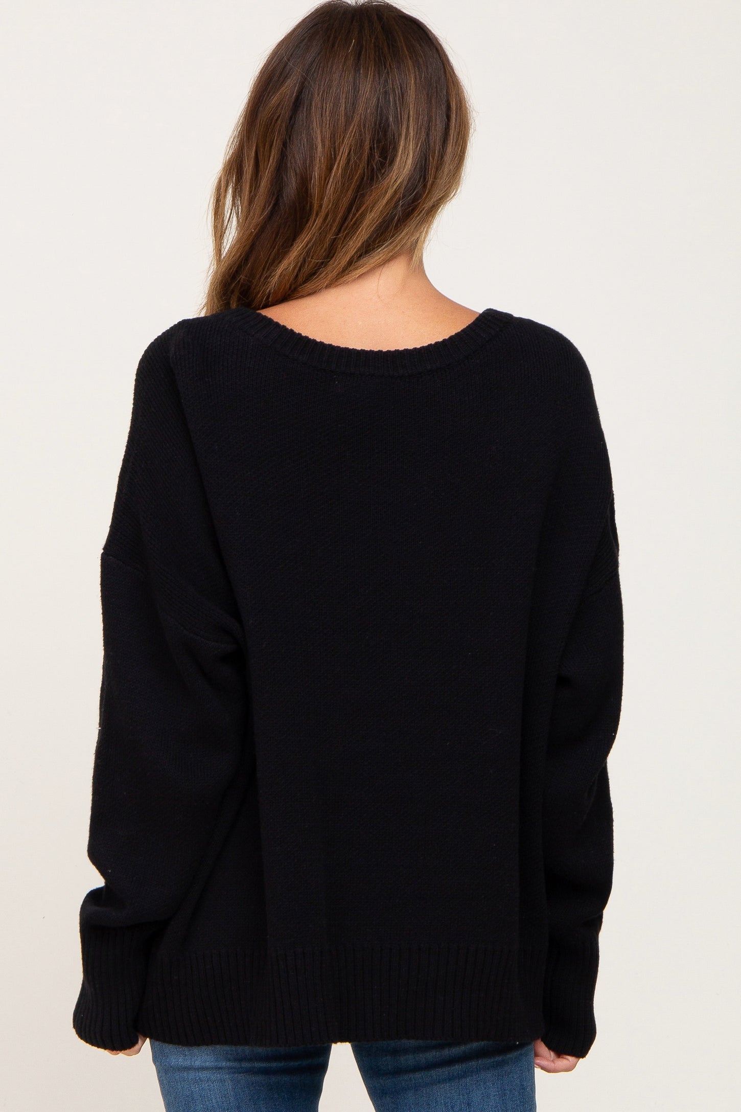 Back view of a woman wearing a black oversized knit sweater with a scoop neckline and ribbed hem.