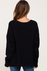 Back view of a woman wearing a black oversized knit sweater with a scoop neckline and ribbed hem.