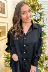 smiling woman wearing a black satin button-down shirt standing in front of a decorated Christmas tree